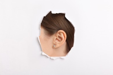 Woman showing her ear through hole in white paper, closeup