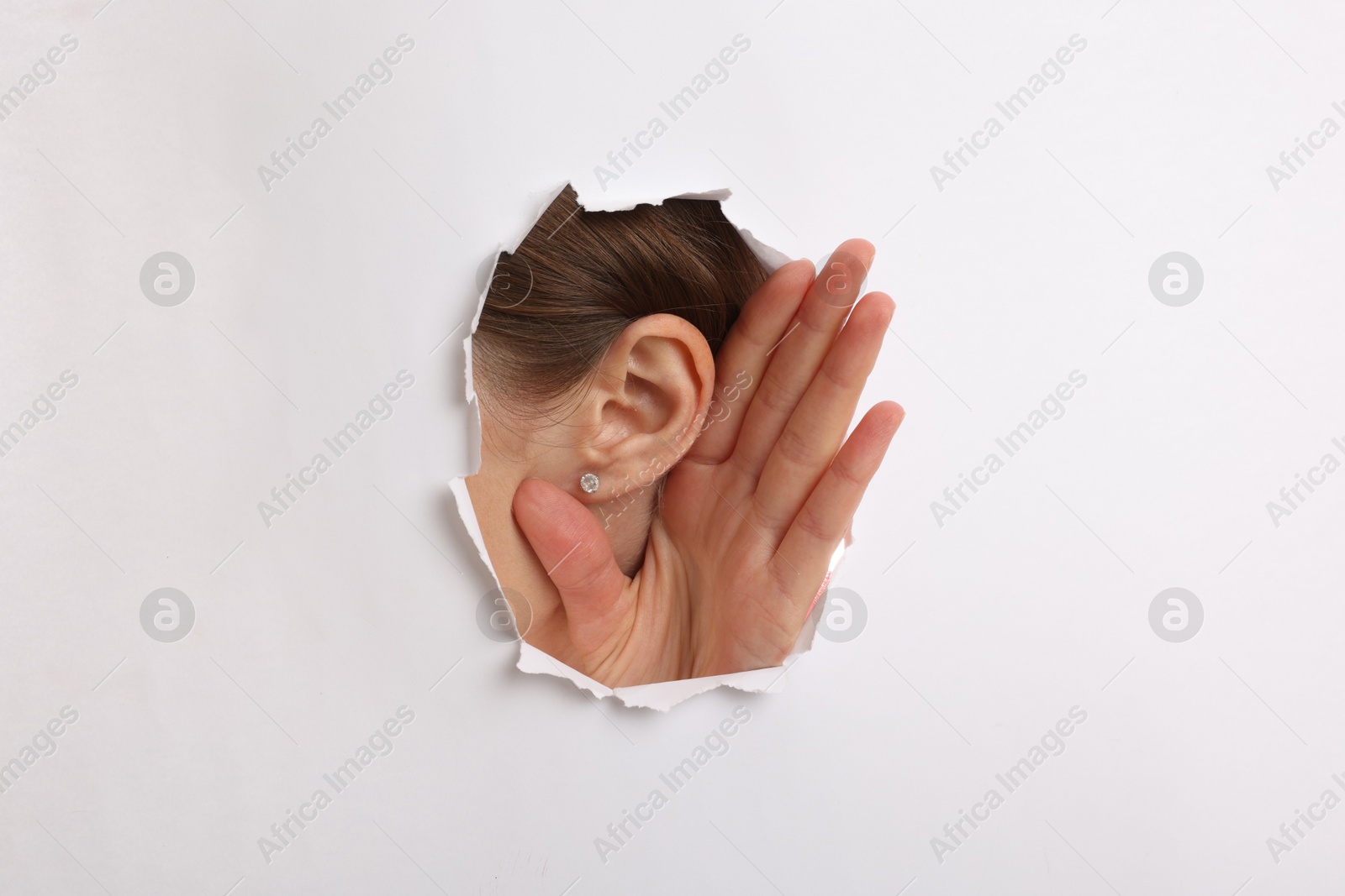 Photo of Woman showing hand to ear gesture through hole in white paper, closeup