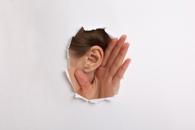 Woman showing hand to ear gesture through hole in white paper, closeup