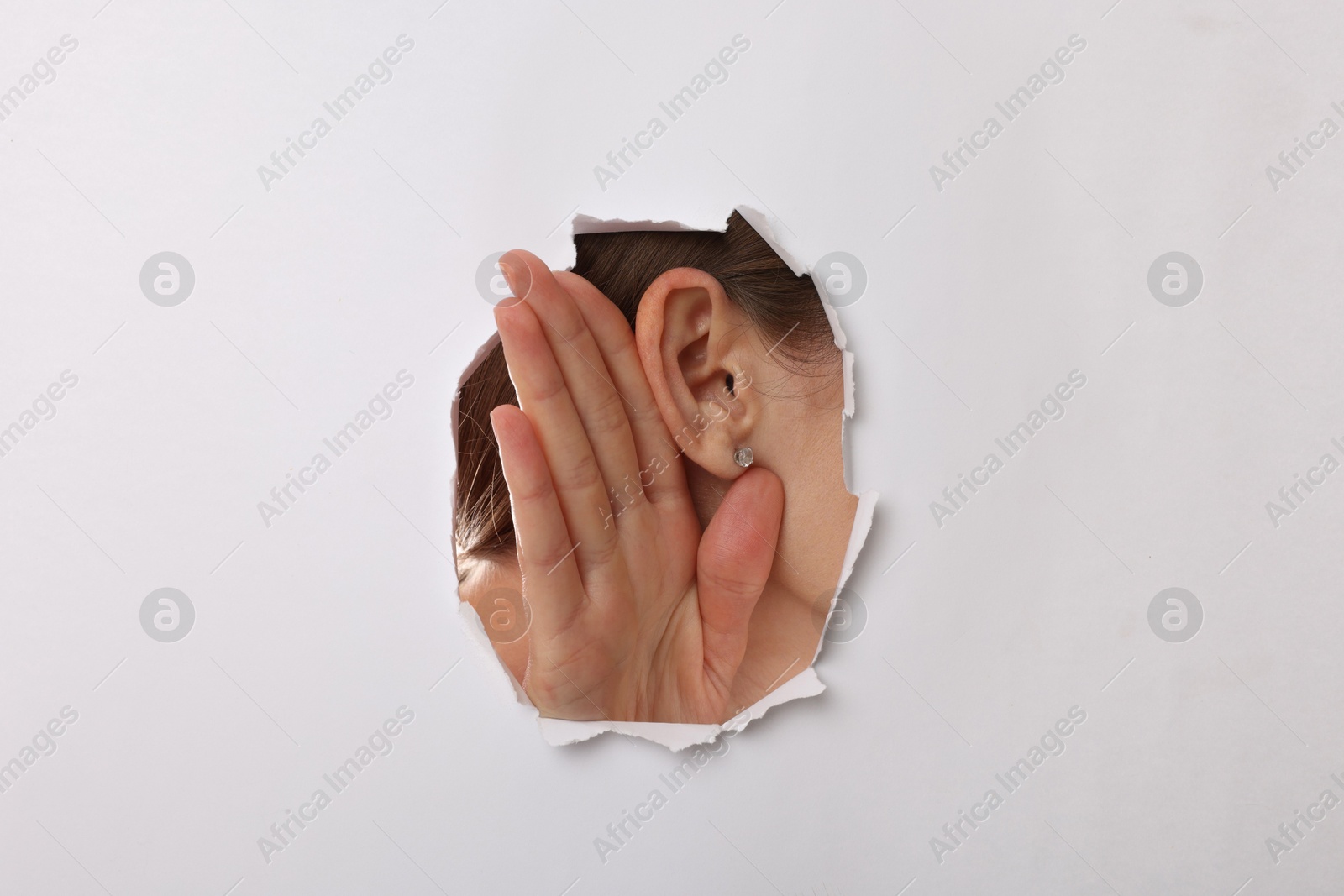 Photo of Woman showing hand to ear gesture through hole in white paper, closeup