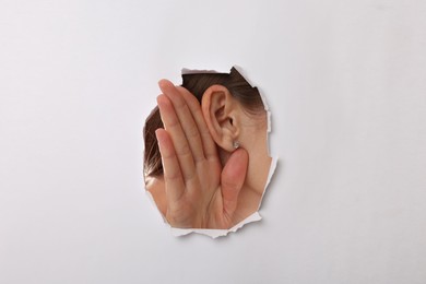 Photo of Woman showing hand to ear gesture through hole in white paper, closeup