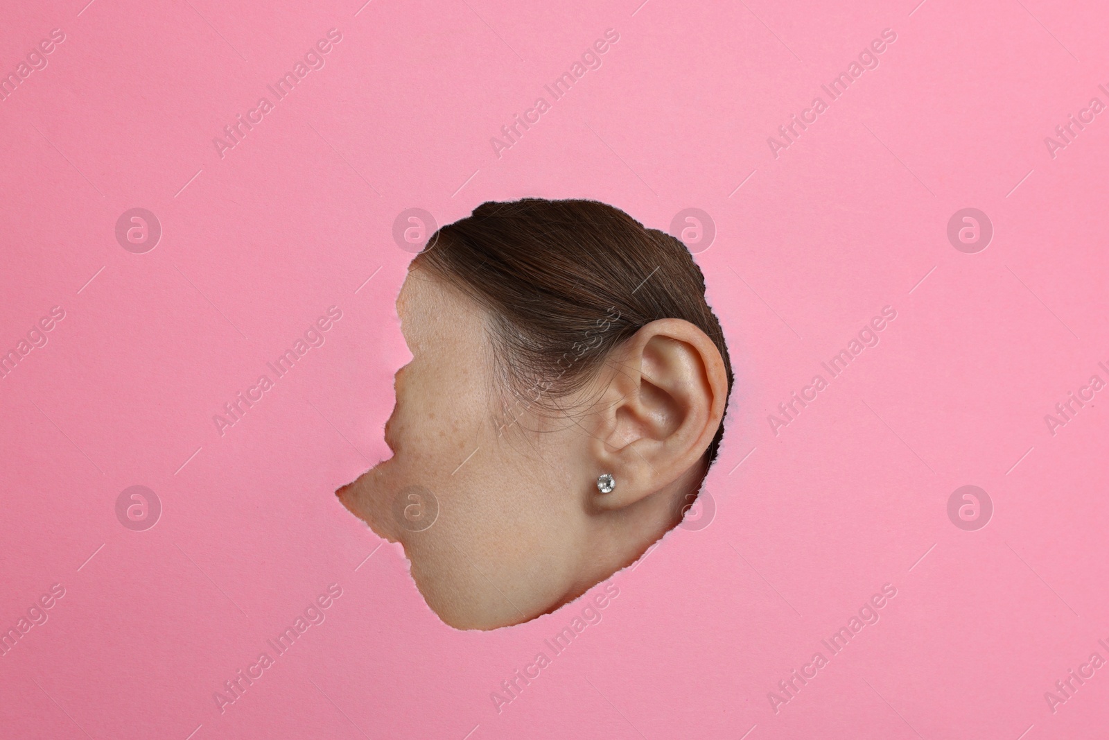 Photo of Woman showing her ear through hole in pink paper, closeup