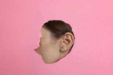 Photo of Woman showing her ear through hole in pink paper, closeup