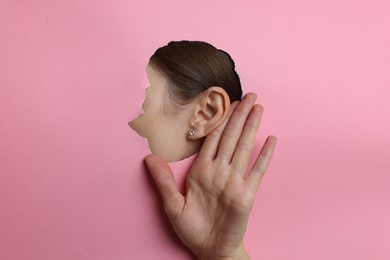 Photo of Woman showing hand to ear gesture through hole in pink paper, closeup