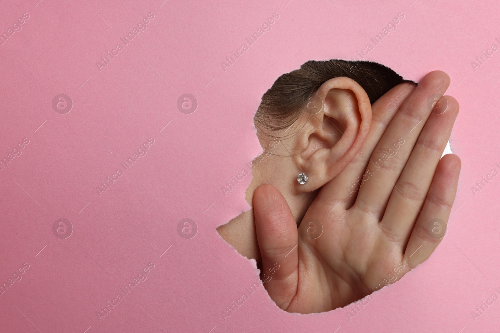 Photo of Woman showing hand to ear gesture through hole in pink paper, closeup. Space for text