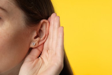 Woman showing hand to ear gesture on dark yellow background, closeup. Space for text