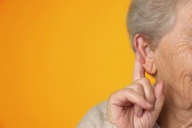 Photo of Senior woman showing hand to ear gesture on dark yellow background, closeup. Space for text