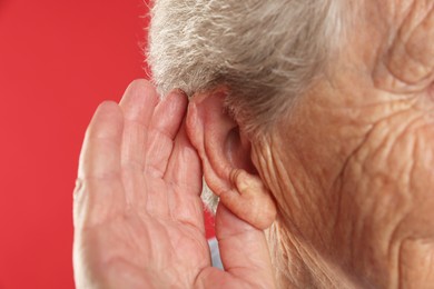 Senior woman showing hand to ear gesture on red background, closeup