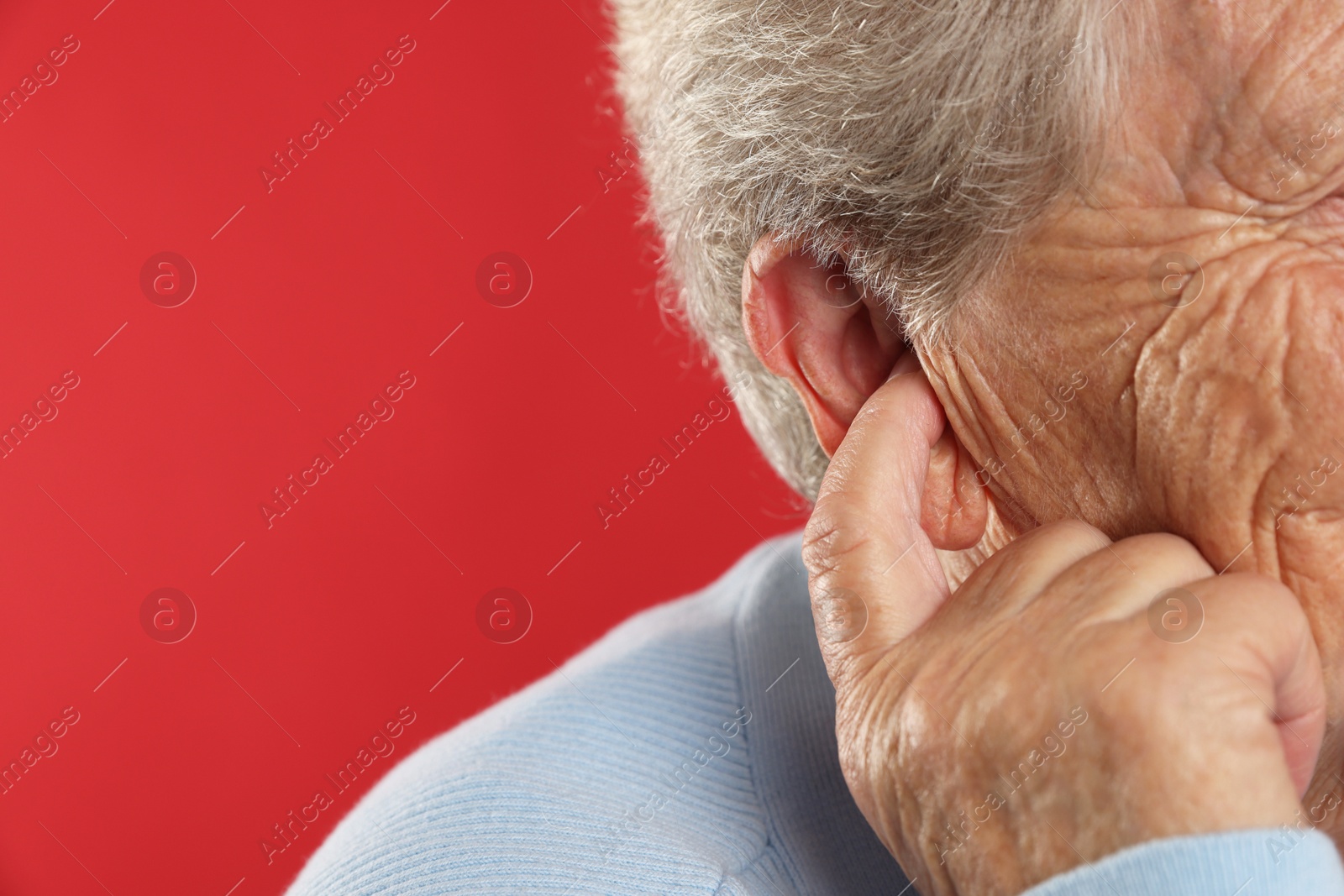 Photo of Senior woman covering her ear with finger on red background, closeup. Space for text