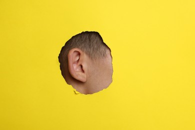 Photo of Man showing his ear through hole in yellow paper, closeup