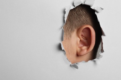 Man showing his ear through hole in grey paper, closeup. Space for text