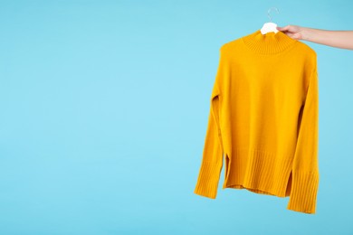 Photo of Woman holding hanger with warm sweater on light blue background, closeup. Space for text