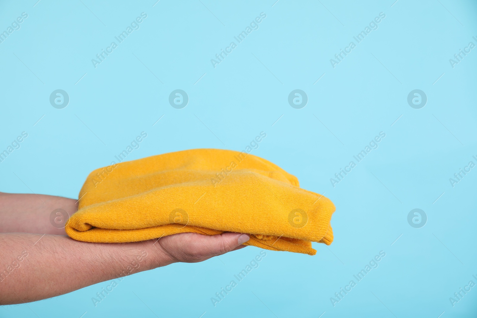 Photo of Woman holding folded sweater on light blue background, closeup. Space for text