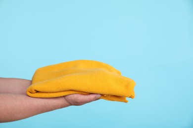 Photo of Woman holding folded sweater on light blue background, closeup. Space for text