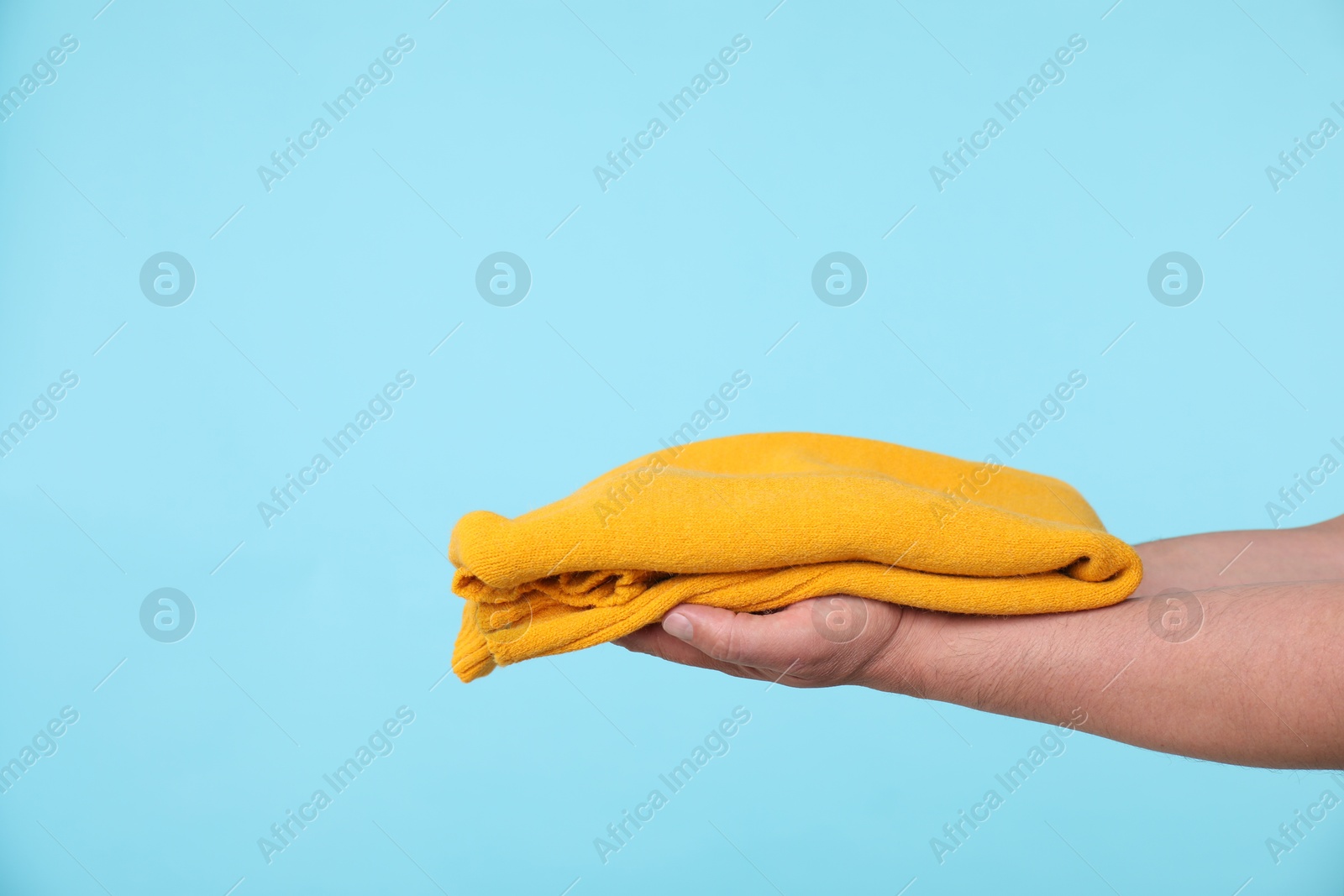 Photo of Woman holding folded sweater on light blue background, closeup. Space for text