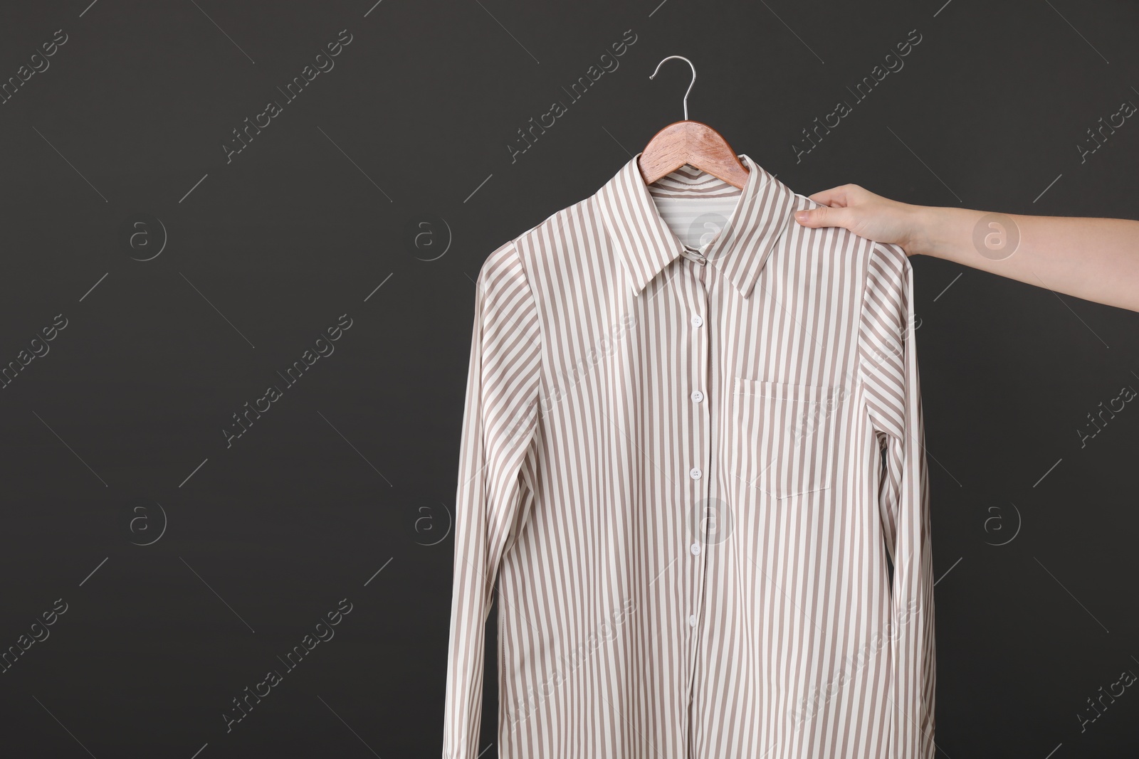 Photo of Woman holding hanger with shirt on black background, closeup. Space for text