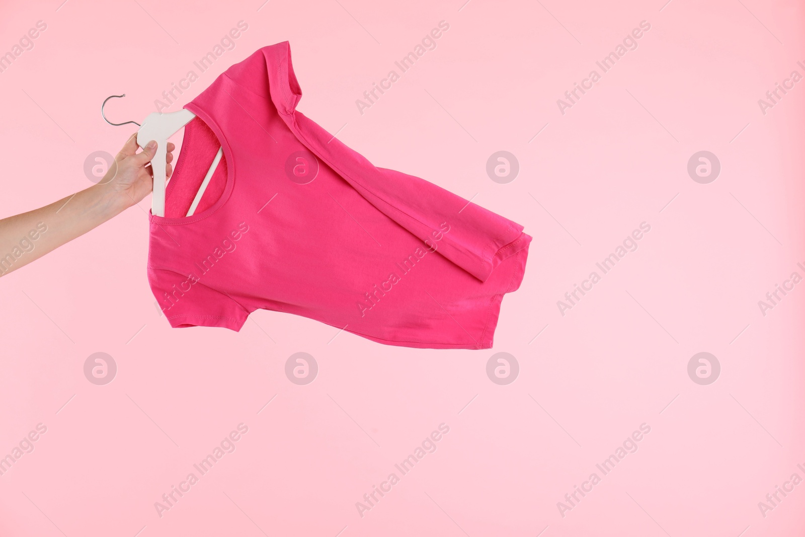 Photo of Woman holding hanger with t-shirt on pink background, closeup. Space for text