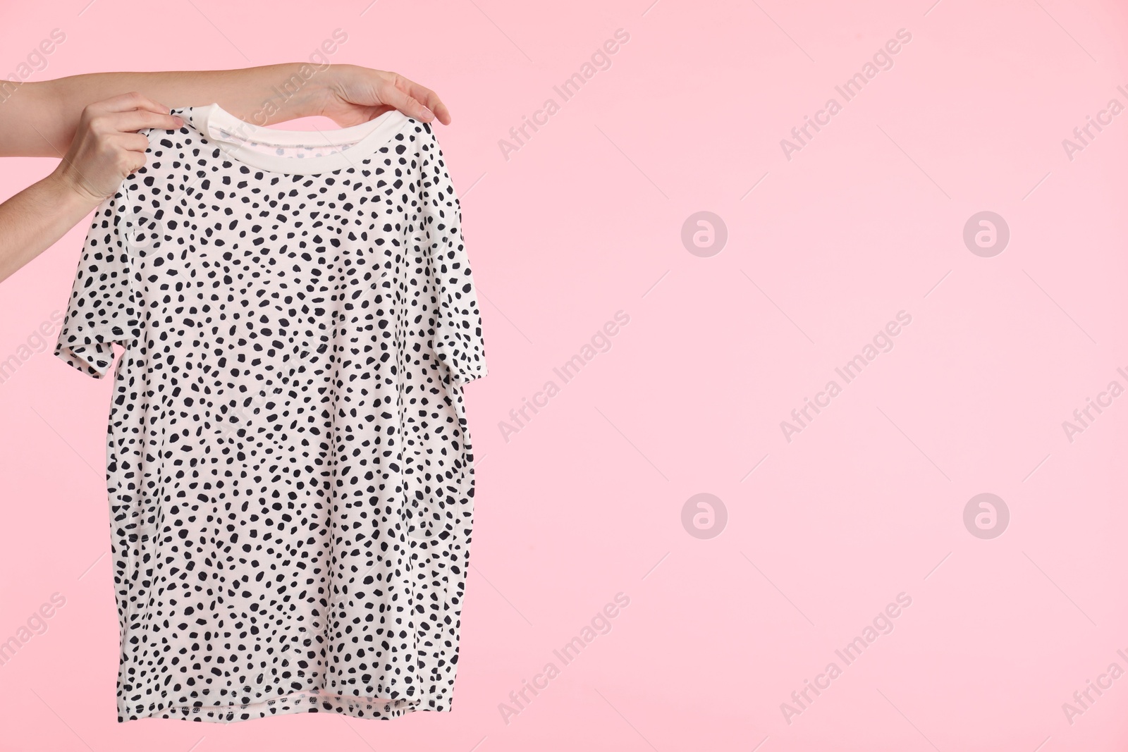 Photo of Woman holding stylish t-shirt on pink background, closeup. Space for text