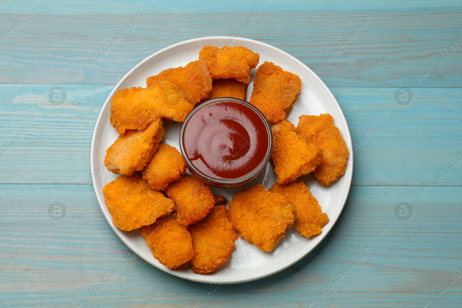 Photo of Delicious chicken nuggets with ketchup on blue wooden table, top view