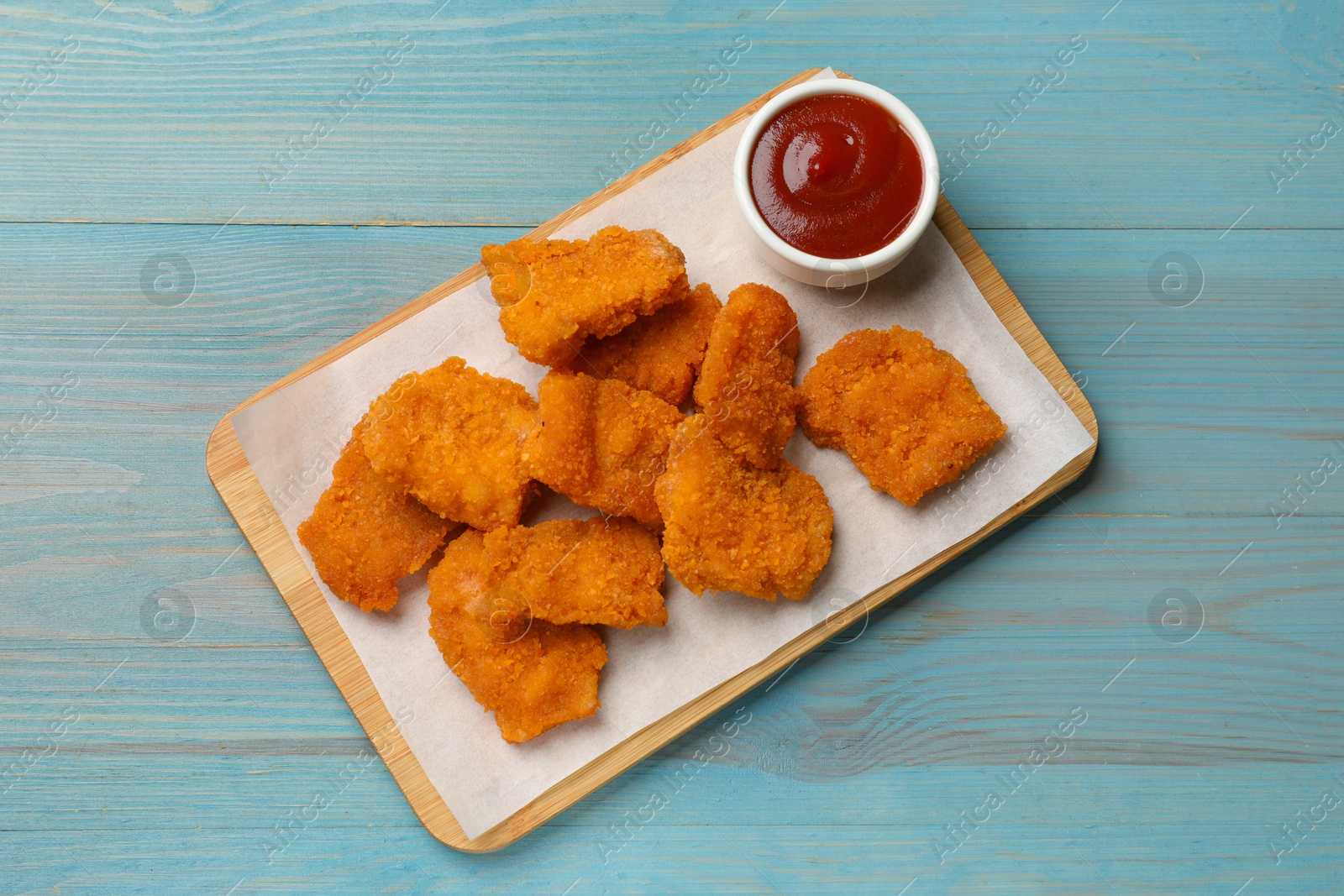 Photo of Delicious chicken nuggets with ketchup on blue wooden table, top view