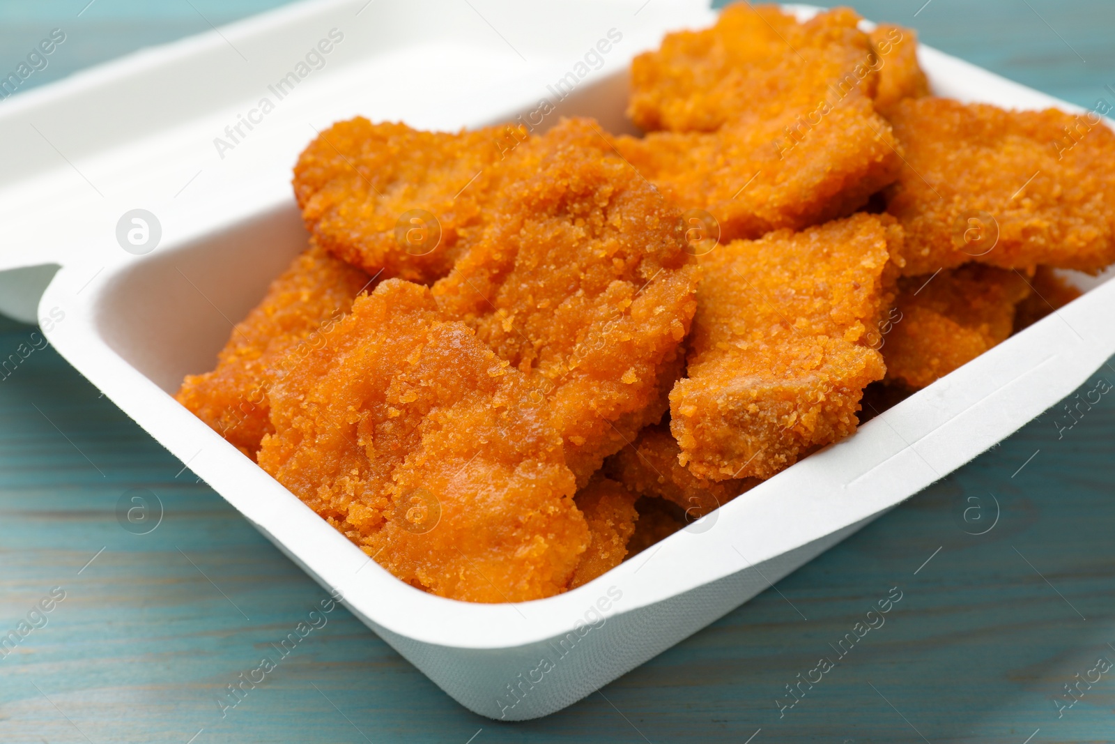 Photo of Delicious chicken nuggets in takeaway container on blue wooden table, closeup