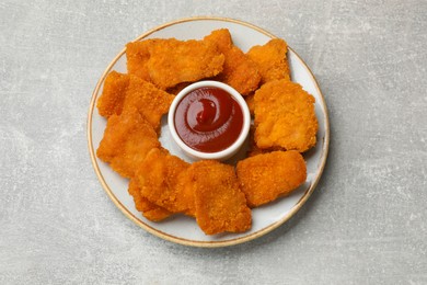 Photo of Delicious chicken nuggets with ketchup on grey textured table, top view