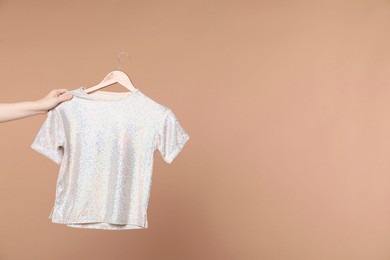 Photo of Woman holding hanger with white t-shirt on beige background, closeup. Space for text