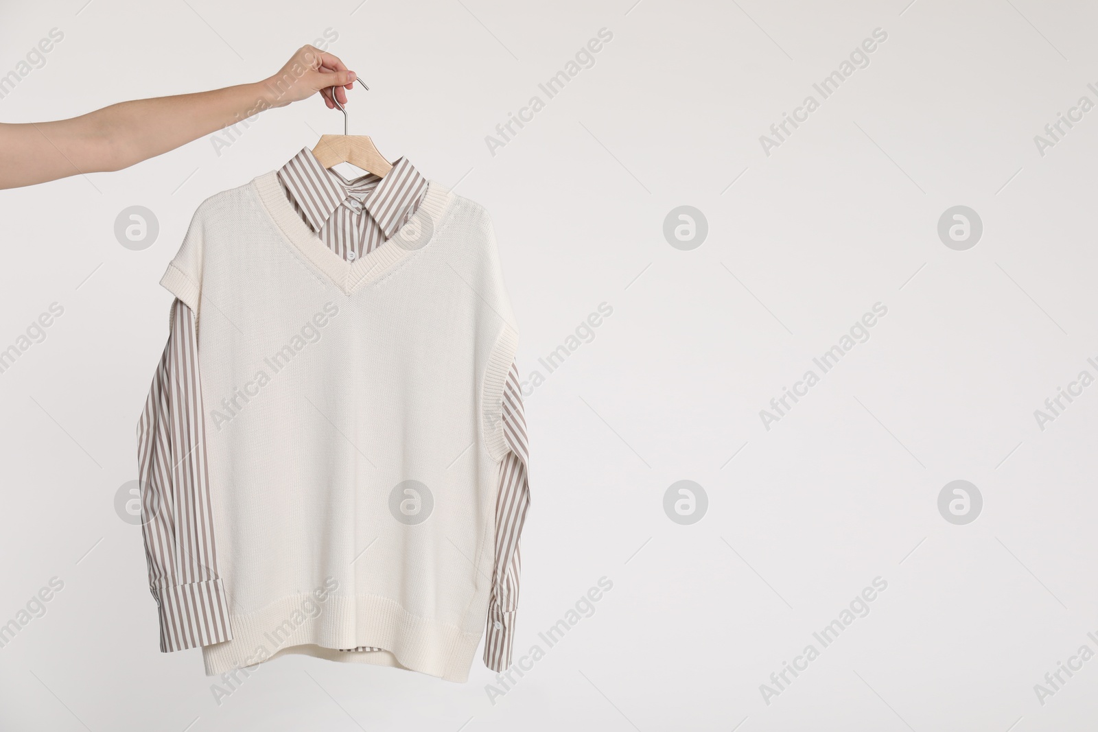 Photo of Woman holding hanger with shirt and sweater vest on white background, closeup