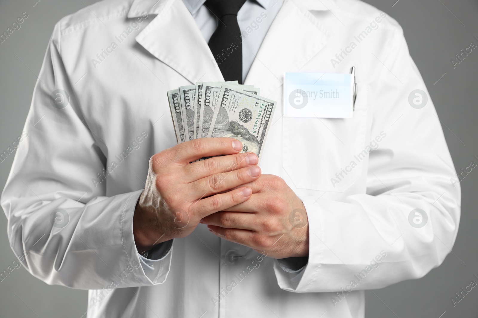 Photo of Corruption concept. Doctor with dollar banknotes on grey background, closeup