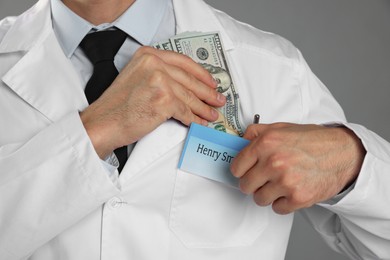 Photo of Corruption concept. Doctor putting dollar banknotes into his pocket on grey background, closeup