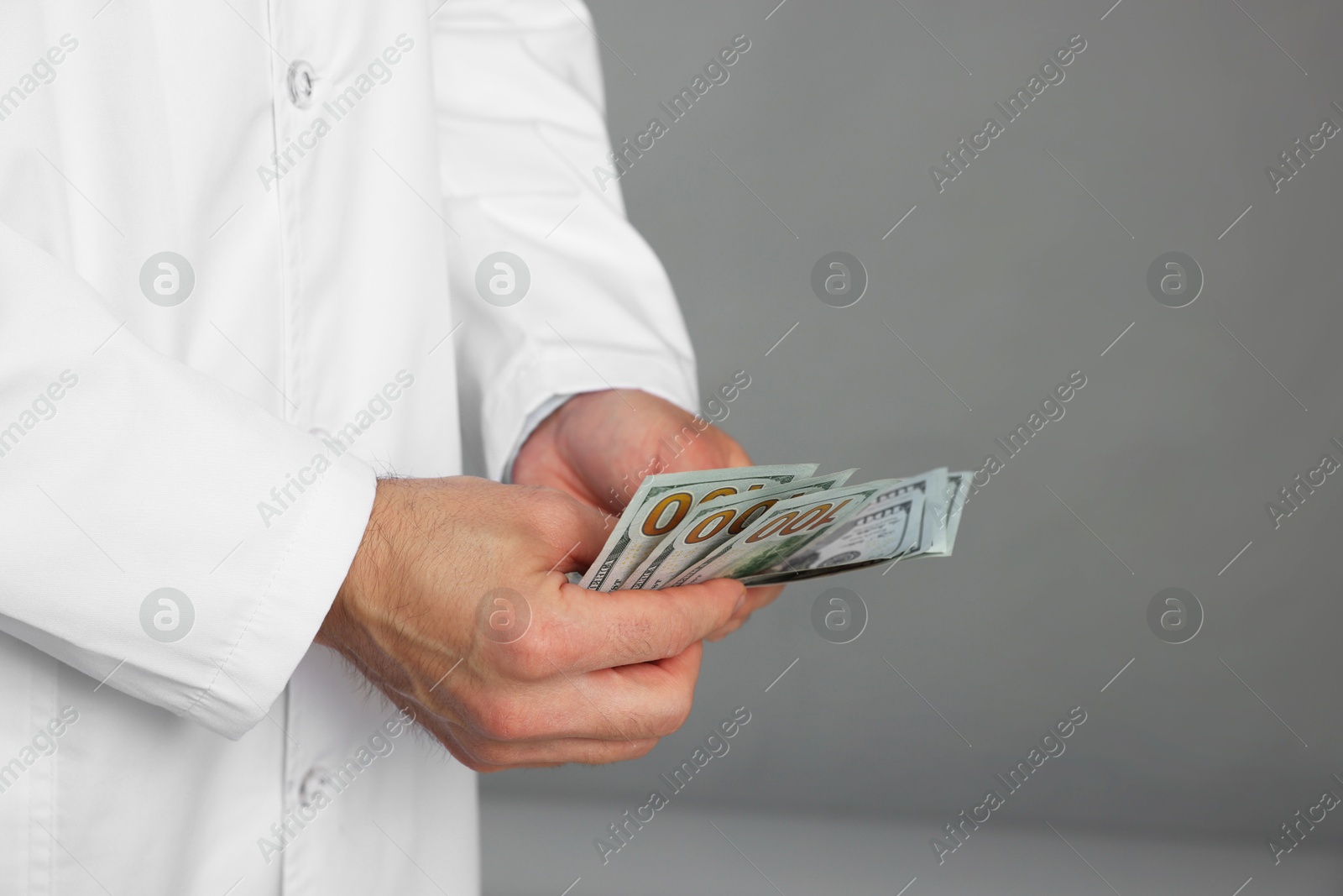 Photo of Corruption concept. Doctor with dollar banknotes on grey background, closeup. Space for text