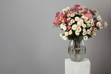 Photo of Vase with beautiful flowers on concrete block against gray background, space for text