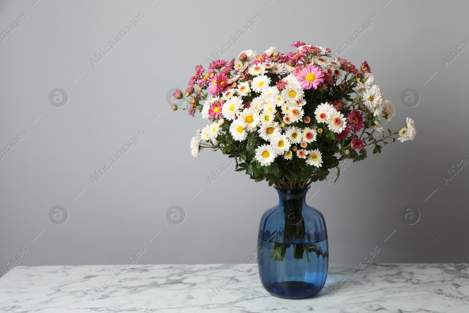 Photo of Vase with beautiful flowers on white marble table against gray background, space for text