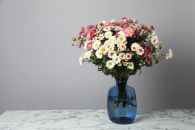 Photo of Vase with beautiful flowers on white marble table against gray background, space for text