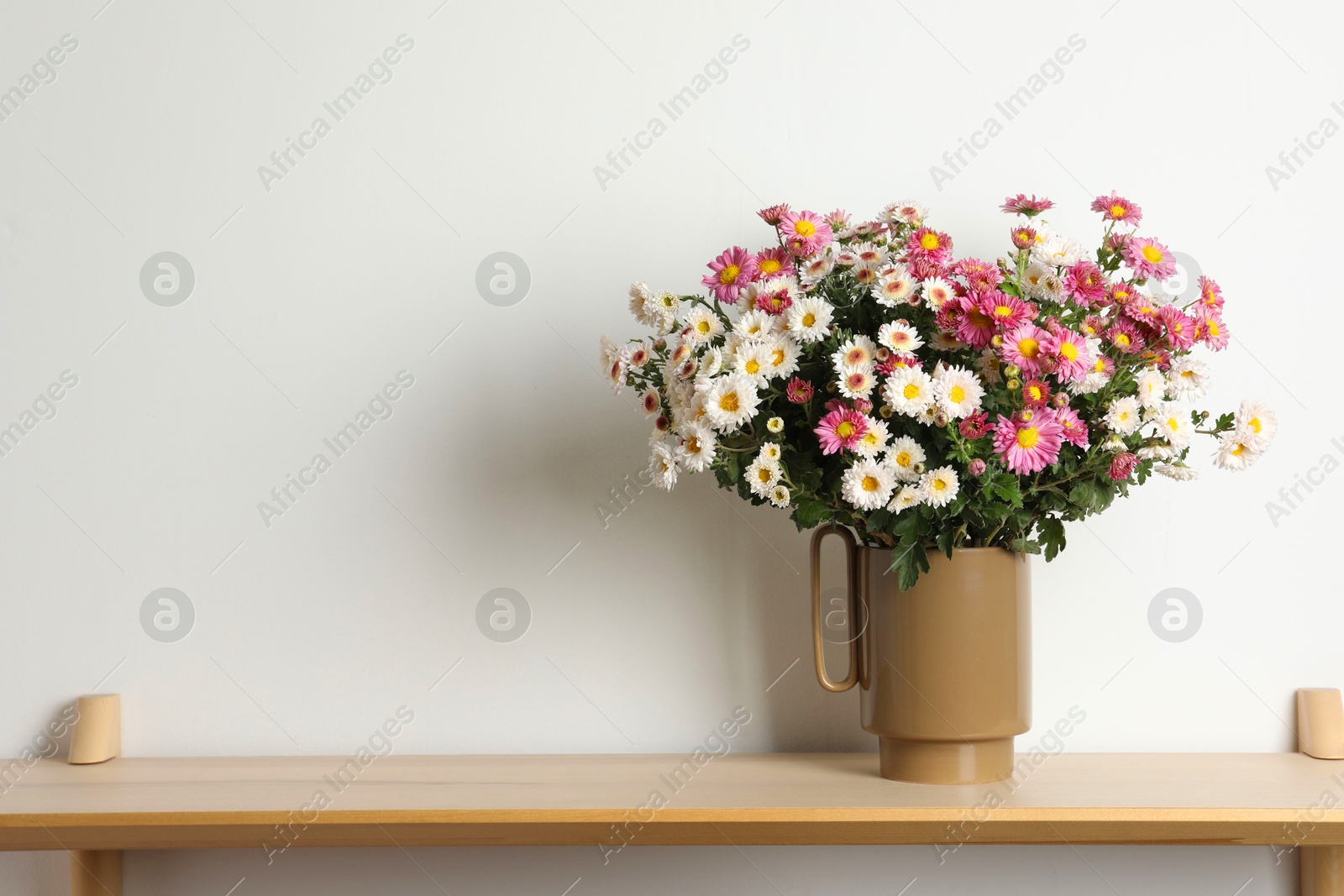 Photo of Vase with beautiful flowers on wooden shelf near white wall, space for text