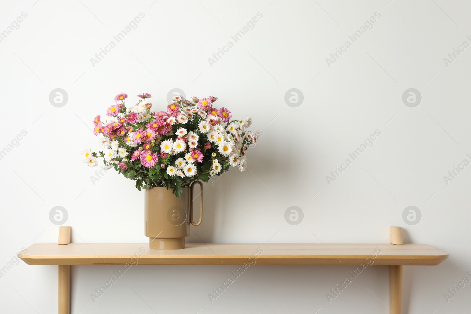 Photo of Vase with beautiful flowers on wooden shelf near white wall, space for text