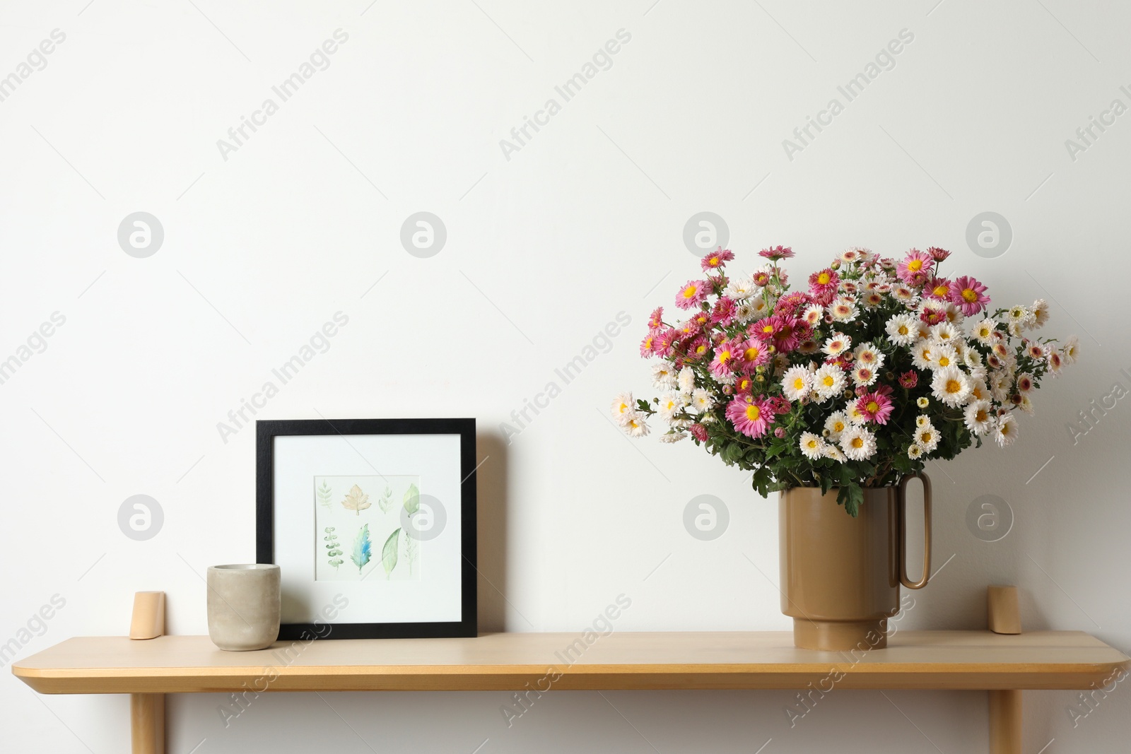 Photo of Vase with beautiful flowers and other decor on wooden shelf near white wall