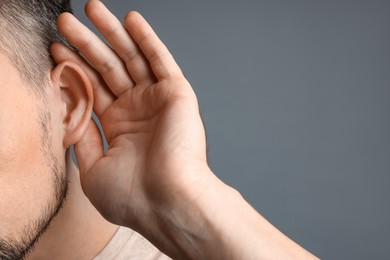 Man showing hand to ear gesture on grey background, closeup