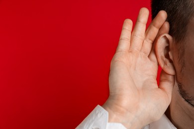 Man showing hand to ear gesture on red background, closeup. Space for text