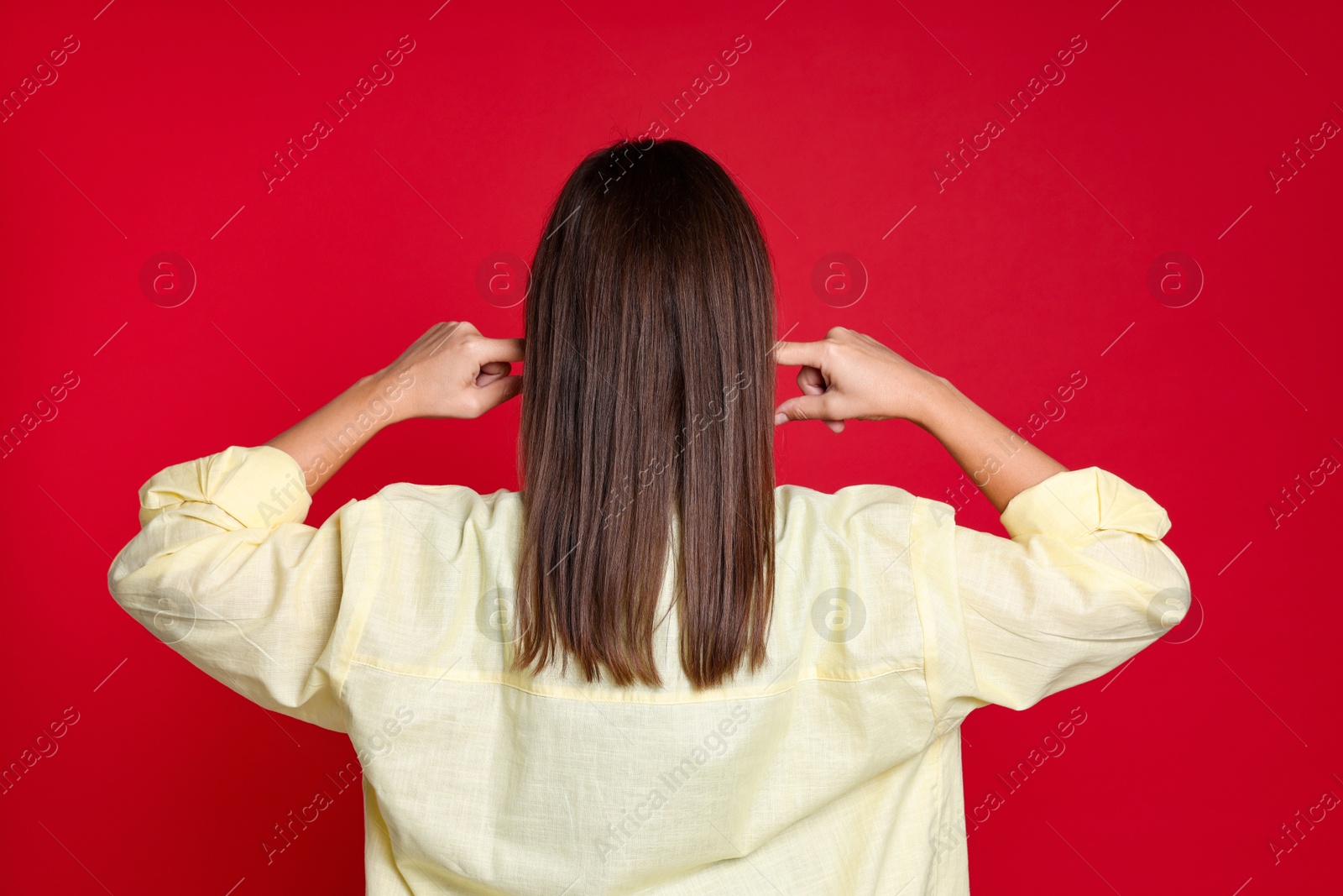 Photo of Woman covering her ears with fingers on red background, back view