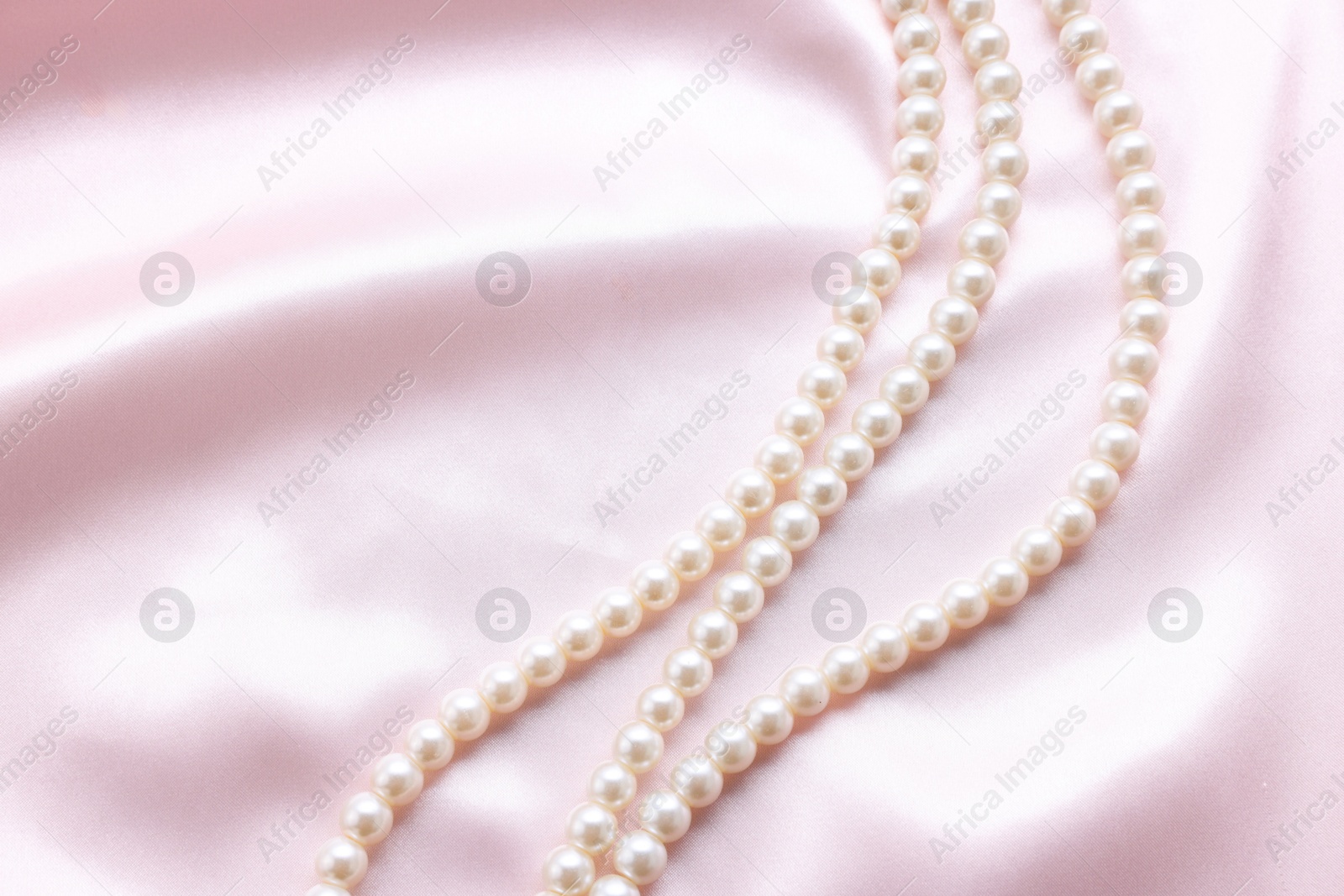 Photo of Elegant pearl necklace on pink fabric, top view. Space for text