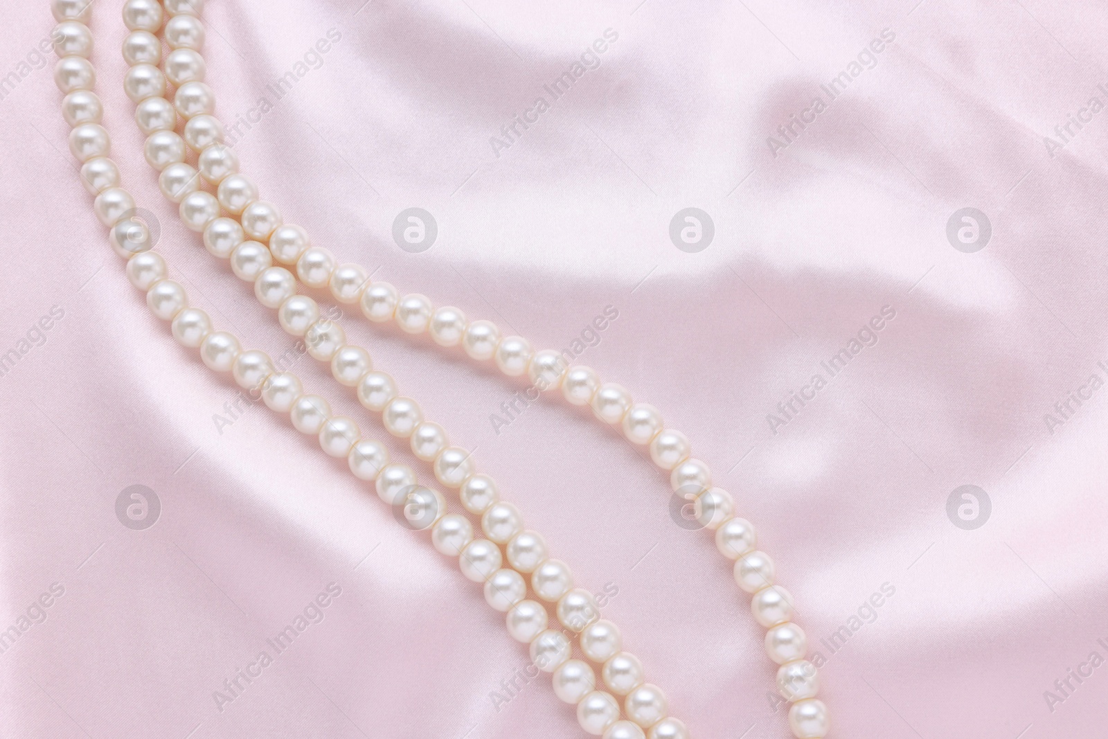 Photo of Elegant pearl necklace on pink fabric, top view. Space for text