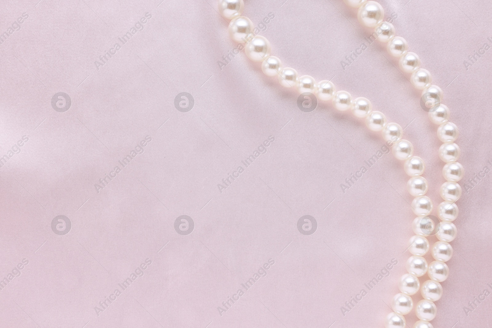 Photo of Elegant pearl necklace on pink fabric, top view. Space for text