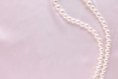 Photo of Elegant pearl necklace on pink fabric, top view. Space for text