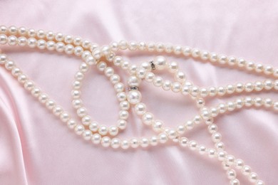 Photo of Elegant pearl necklace on pink fabric, top view