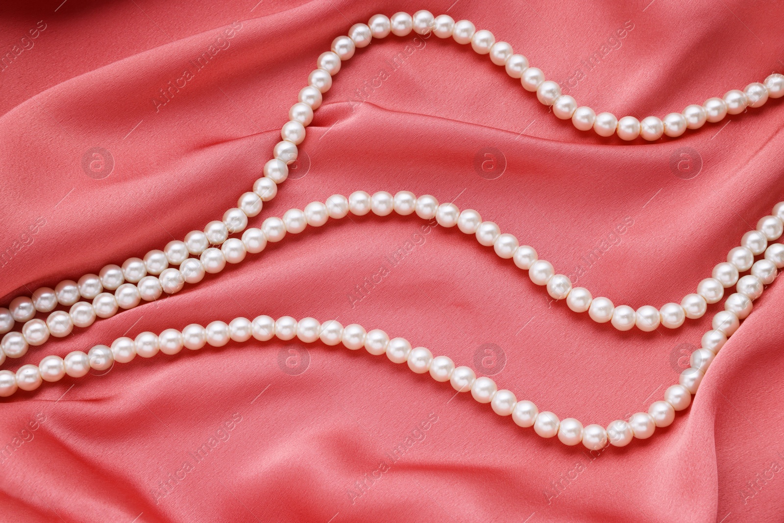 Photo of Elegant pearl necklace on pink fabric, top view