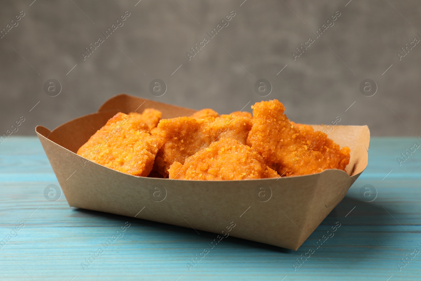 Photo of Delicious chicken nuggets in carton box on light blue wooden table, closeup