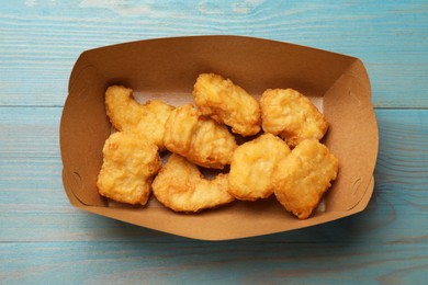 Photo of Delicious chicken nuggets in carton box on light blue wooden table, top view