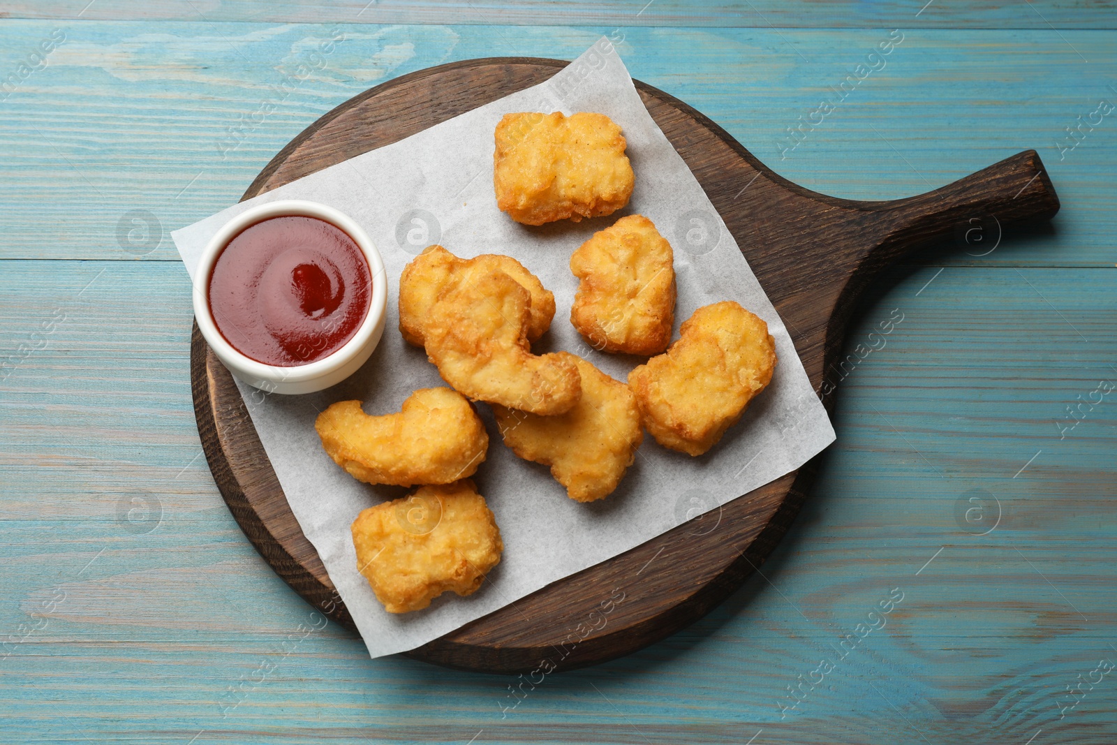 Photo of Delicious chicken nuggets and ketchup on light blue wooden table, top view