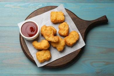 Photo of Delicious chicken nuggets and ketchup on light blue wooden table, top view